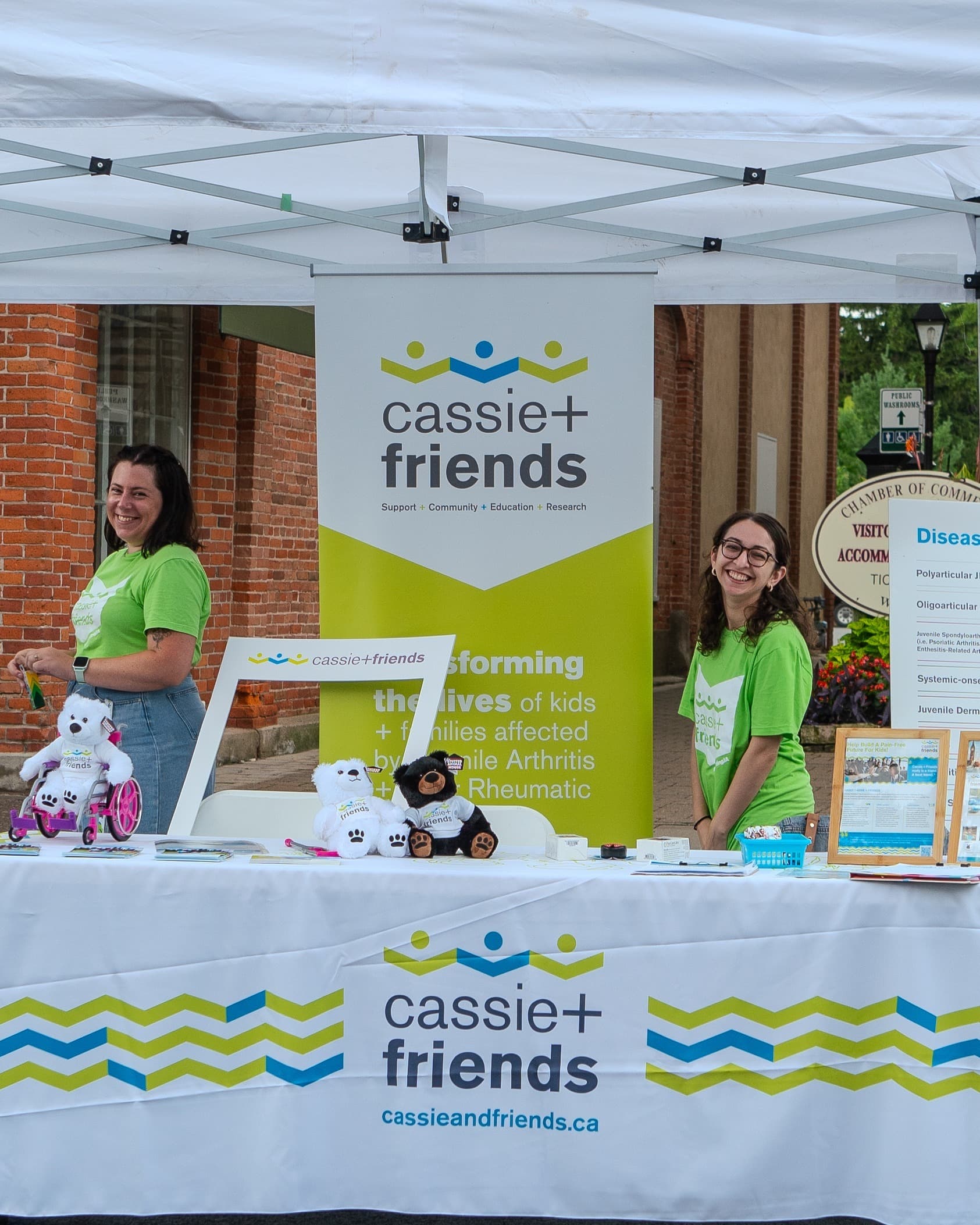 Two volunteers staff a Cassie+Friends charity booth under a white tent