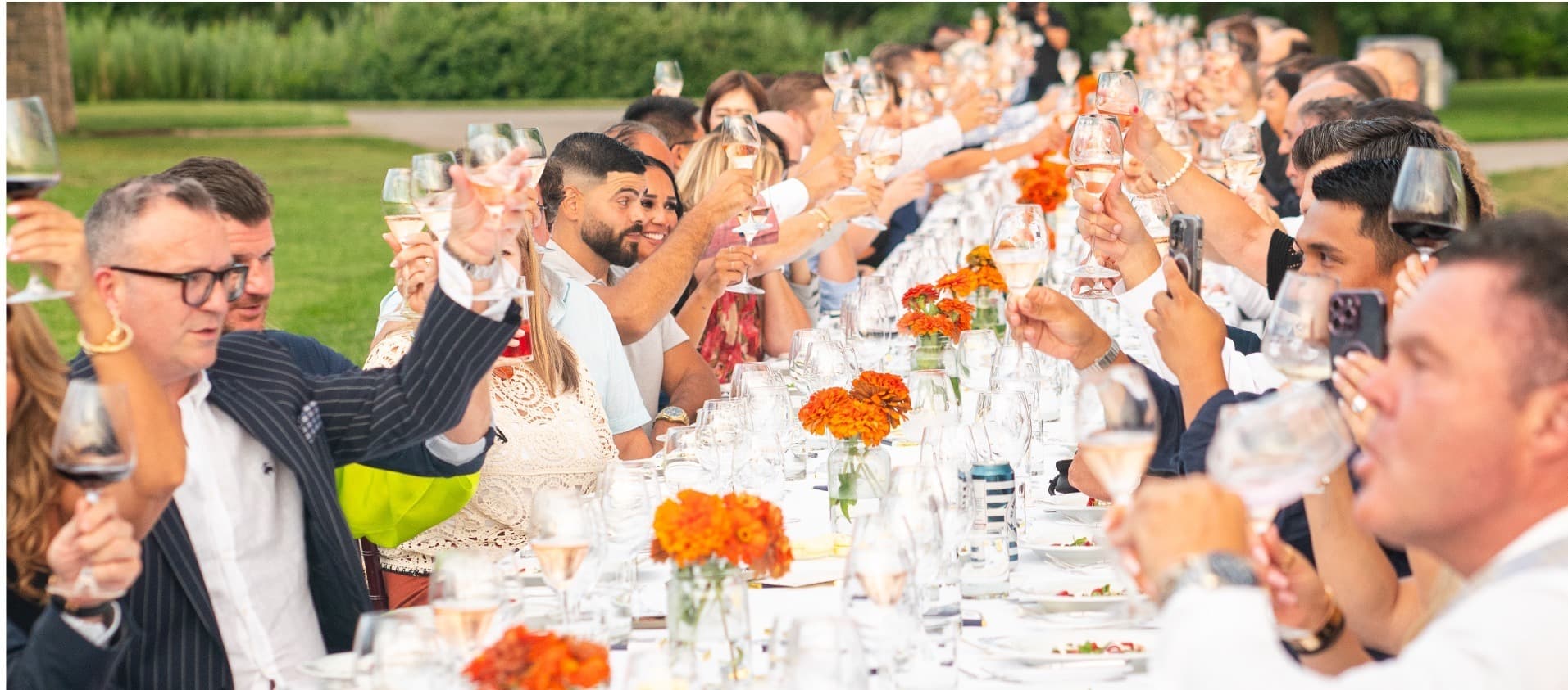 Guests raise wine glasses in a toast at an outdoor long-table winery dinner
