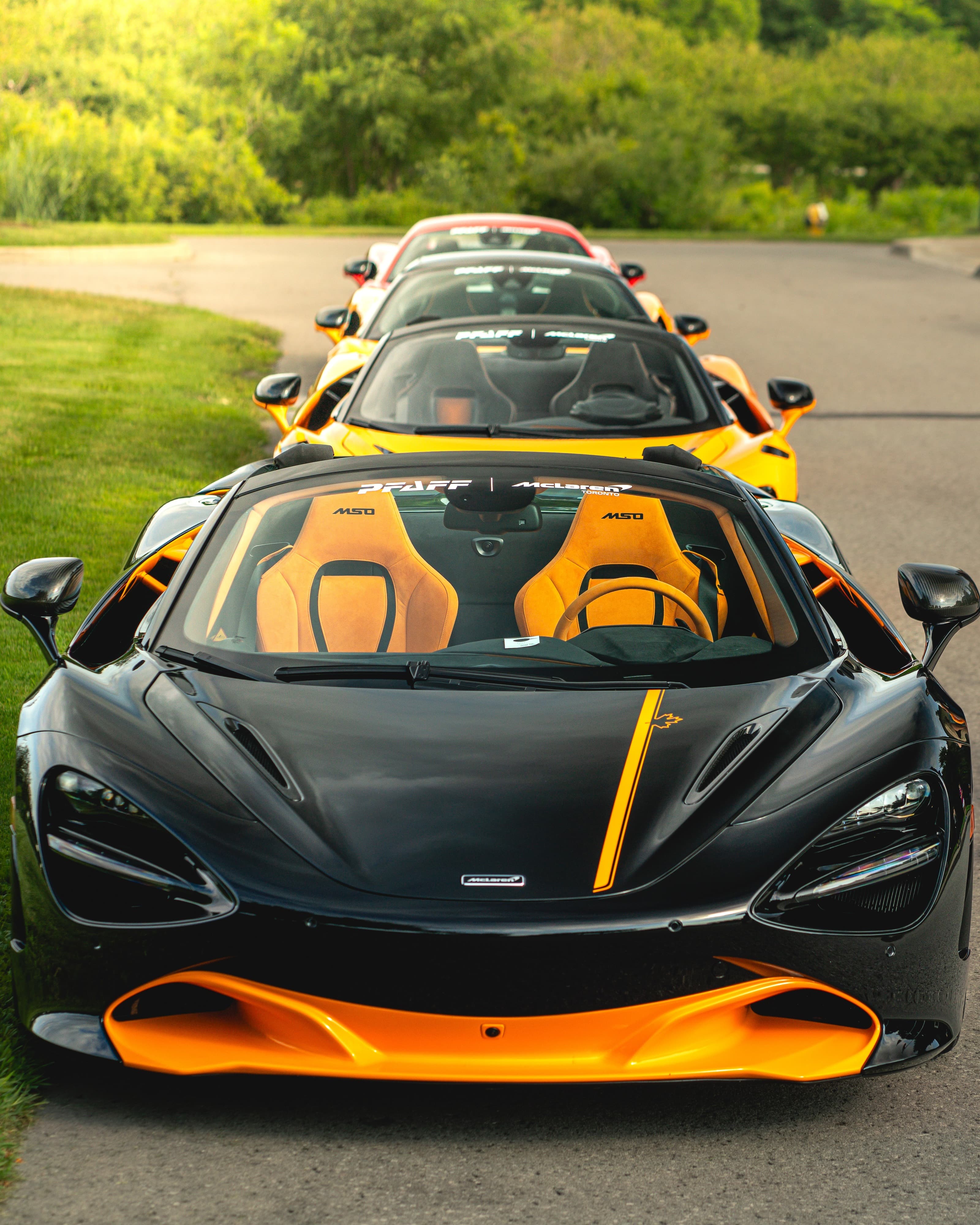 Four McLaren supercars lined up nose-to-tail on a tree-lined road