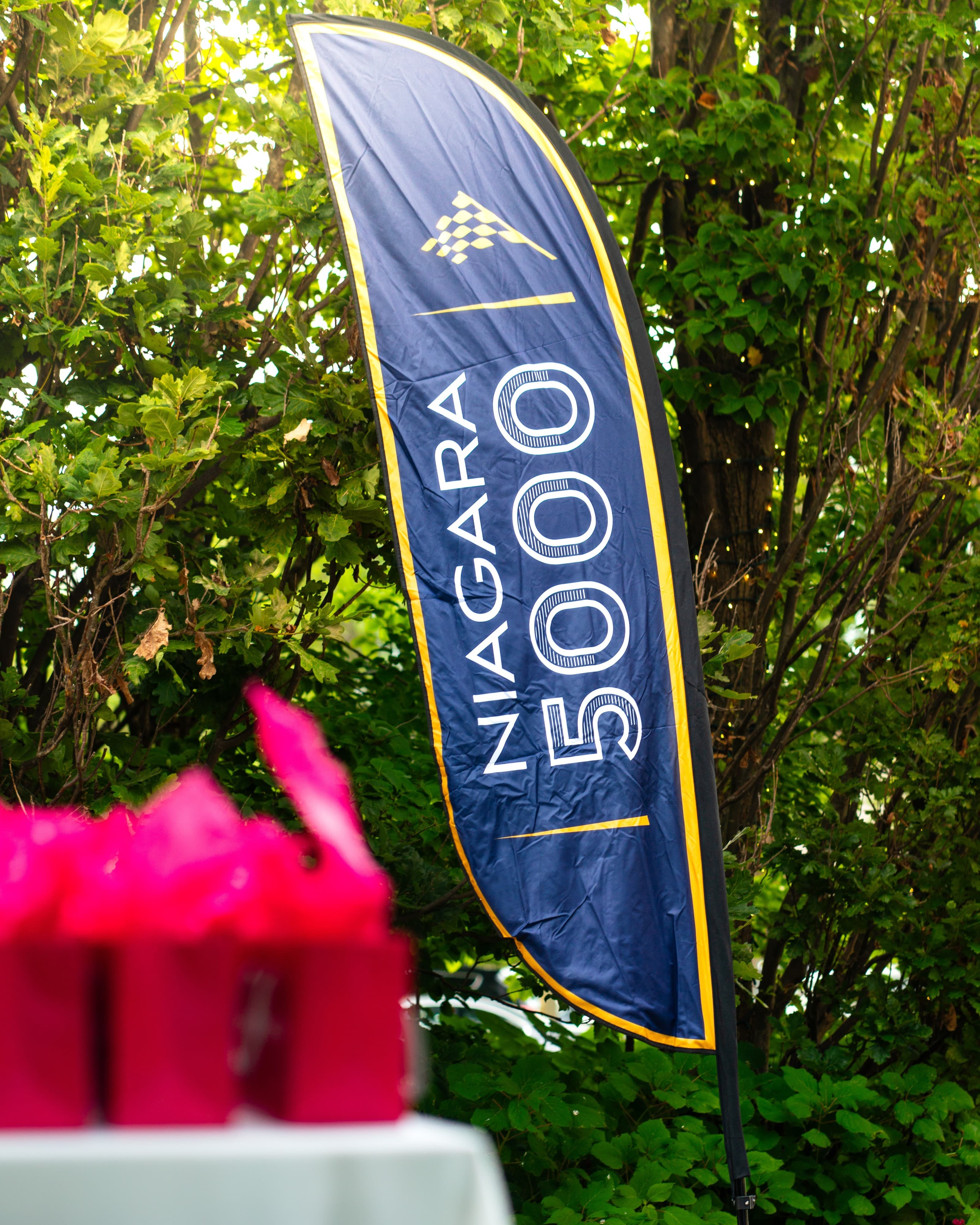 Niagara 5000 branded feather flag standing beside a leafy hedge
