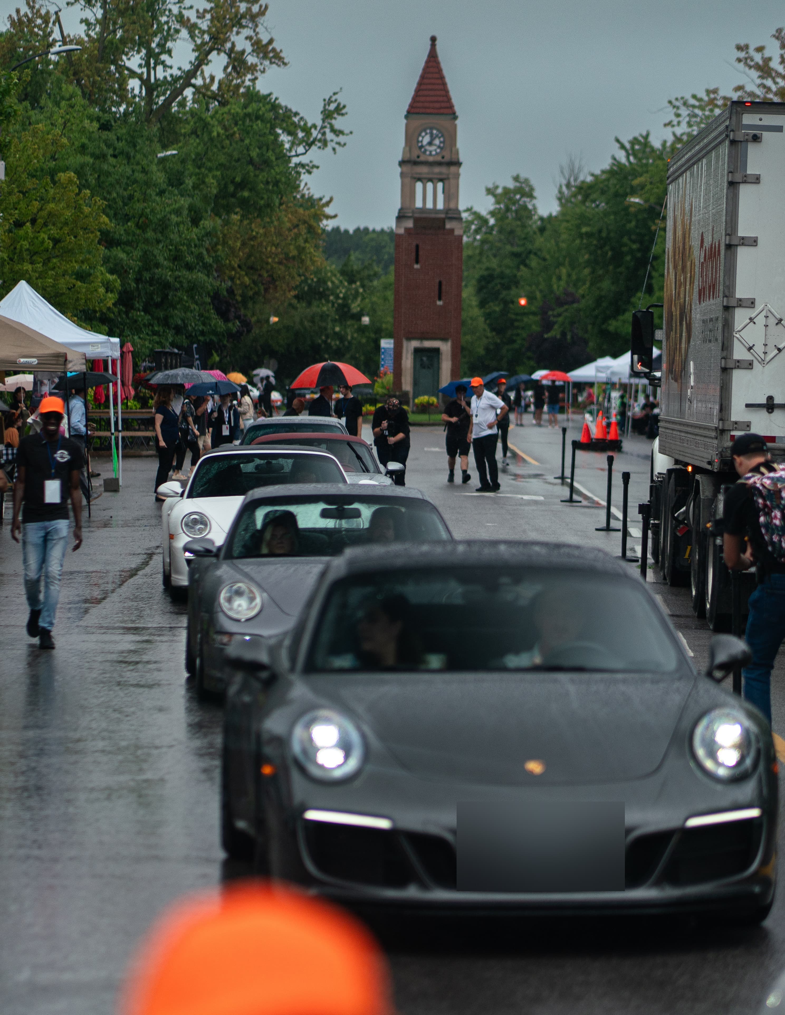 Porsche sports cars queue past the clock tower in rainy Niagara-on-the-Lake