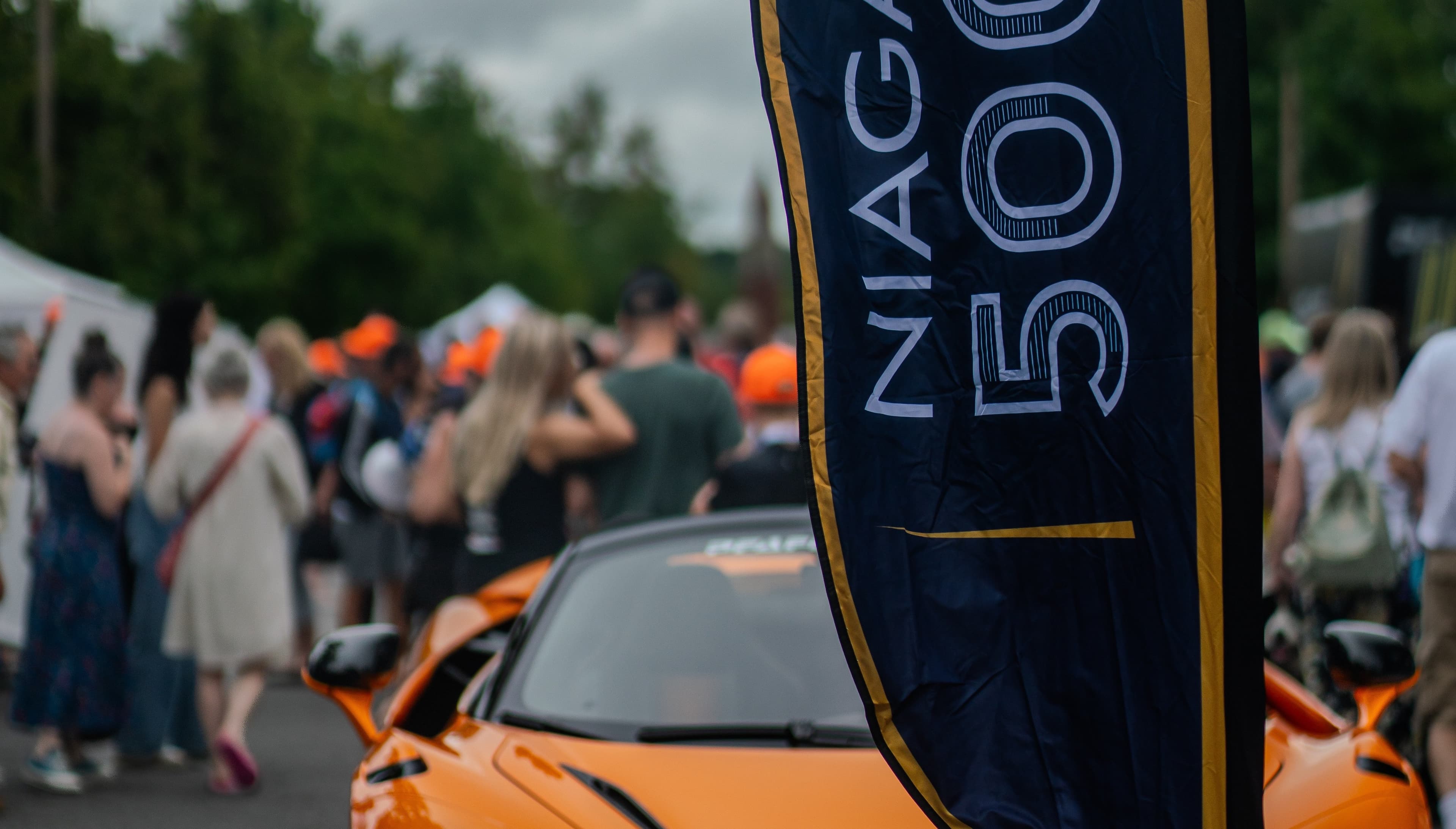 Orange supercar beside a Niagara 5000 event banner amid strolling crowds