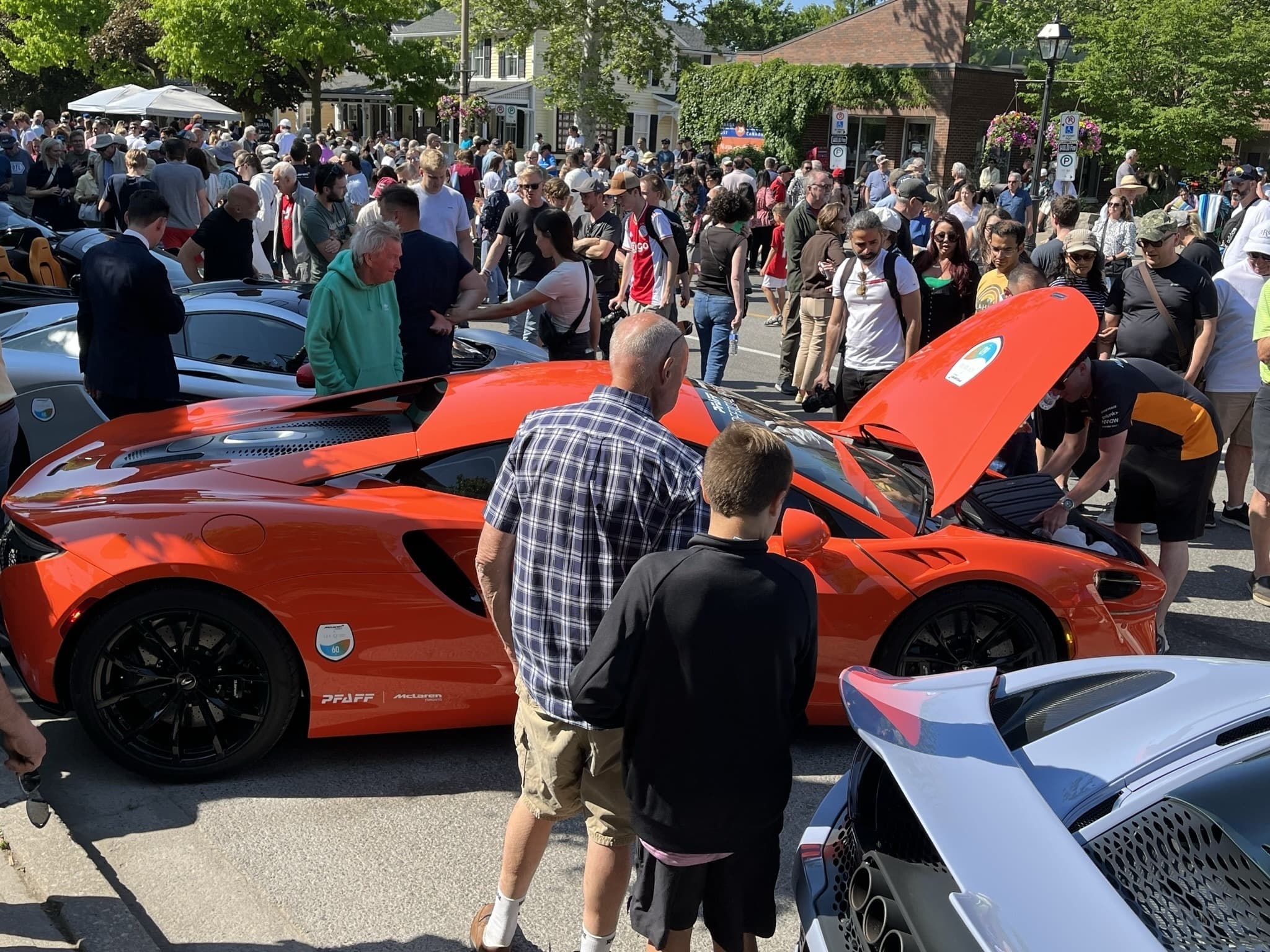 Crowd inspecting an orange McLaren with open hood at a street supercar show