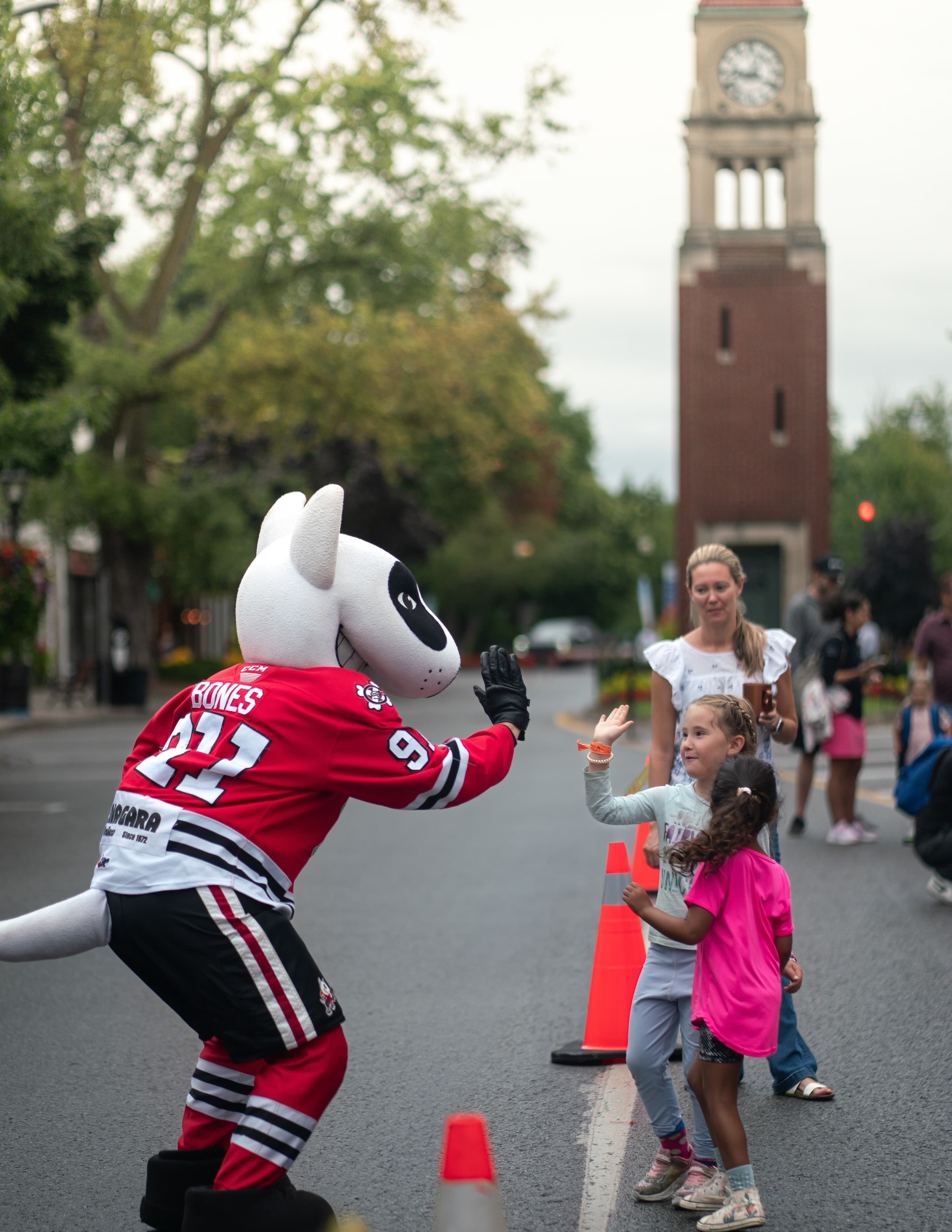 Team mascot high-fives young fans on closed street by clock tower